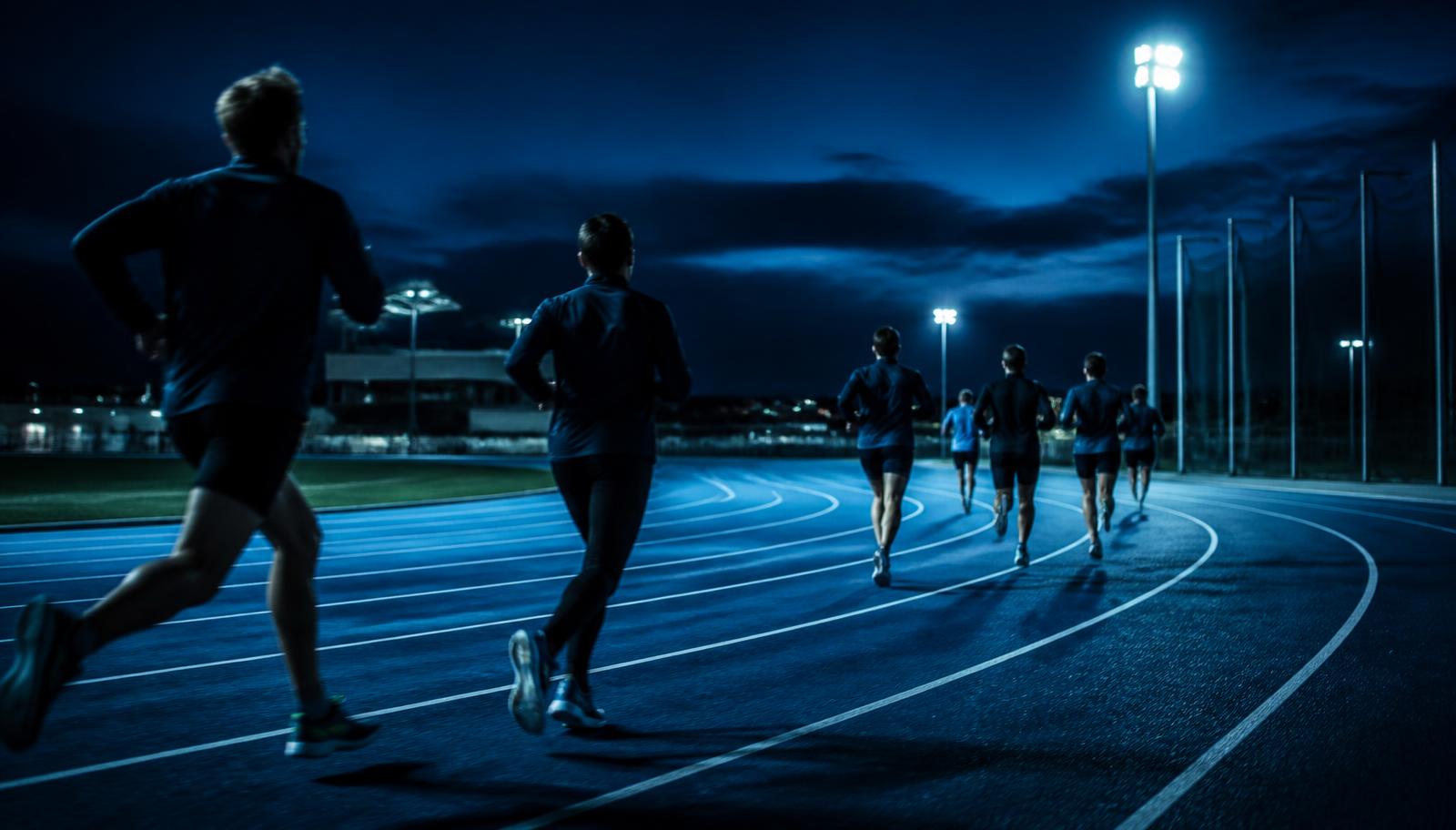 Atletas entrenando en una pista de atletismo iluminada al atardecer